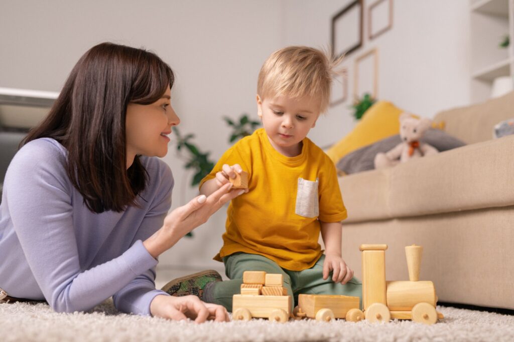 A mother and her toddler are playing with wooden blocks together on the floor at home