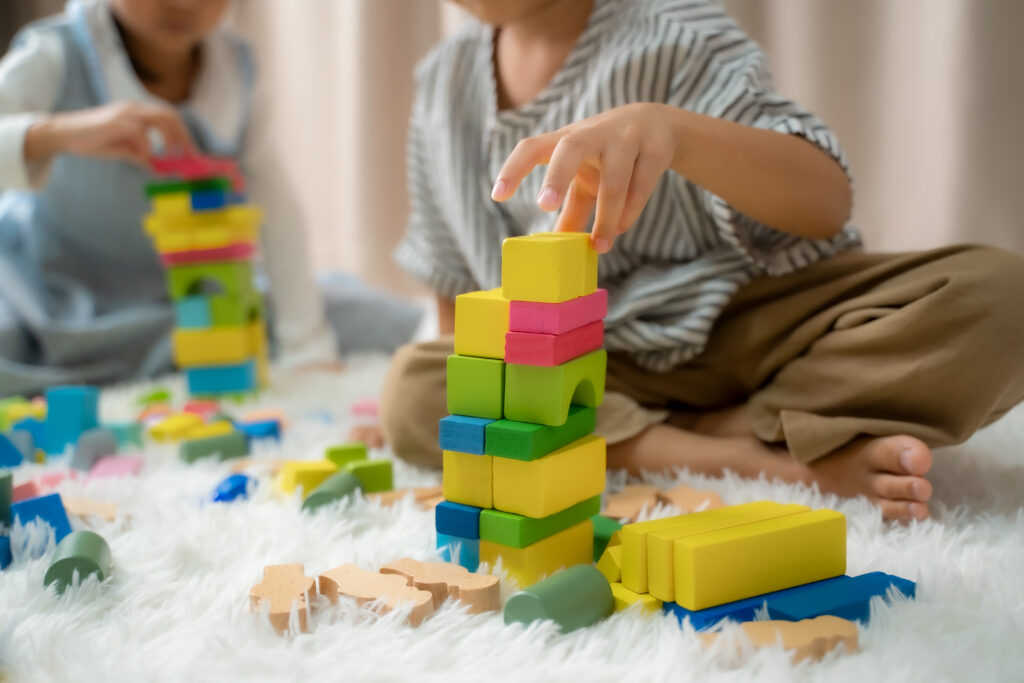 Two children playing side by side with wooden blocks, learning to play together